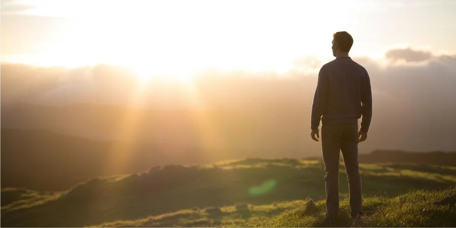 Person looking at a golden sunrise symbolizing hope and peace, illustrating Bible verses about confidence and the reward of righteousness.