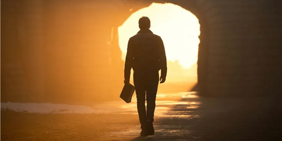 A person walking from dark shadows into bright sunlight holding a Bible, illustrating the pivot in bible verses about shame.