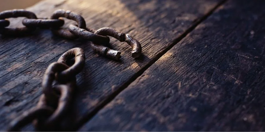 A broken iron chain in warm light, symbolizing Bible verses about your worth and redemption in Christ.